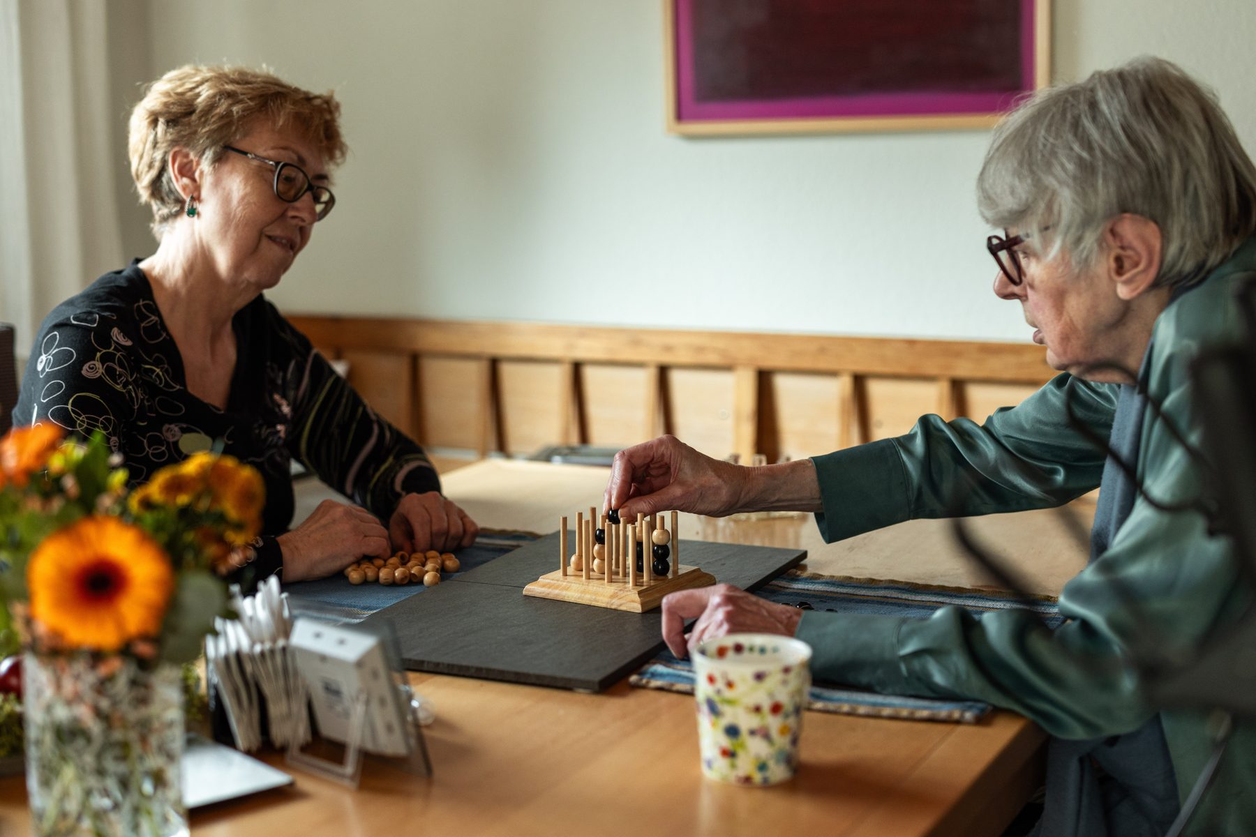 Eine Betreuungskraft spielt mit einer Seniorin am Esstisch ein Steckspiel